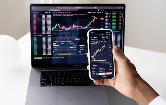 person looking at stock graphs on computer and phone