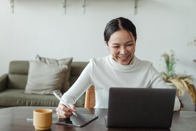 person smiling at laptop in a living room writing on a tablet